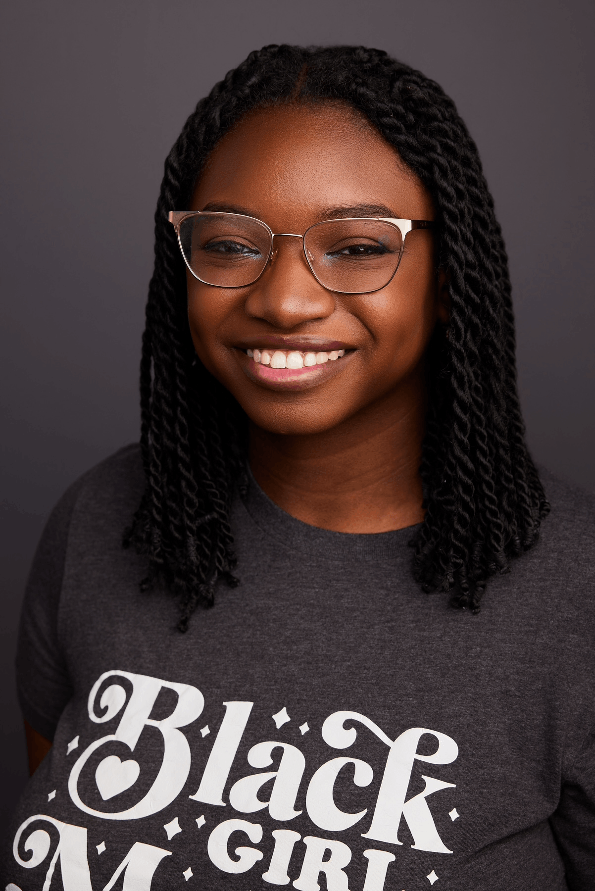a headshot of myself smiling, and wearing glasses and a shirt that reads 'black girl magic'